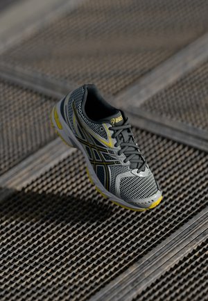 Baskets de course en maille grises avec un motif texturé, des accents jaunes, une forme incurvée et un col rembourré avec des lacets noirs.