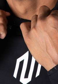 Mani che sistemano il colletto di un felpa nera con un logo geometrico bianco sul petto.
