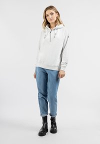 Felpa grigia chiara con zip e coulisse, indossata sopra jeans larghi blu e stivali neri chunky, caratterizzata da una vestibilità rilassata e polsini a coste.