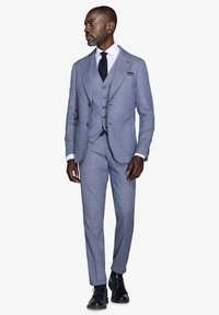Tre-delte lysblå ternet jakkesæt med dobbeltradet jakke, notch-lapel og slim-fit bukser; komplementeret af en hvid skjorte og en mørk slips.