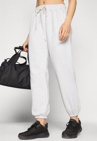 Pantaloni della tuta in cotone grigio chiaro, con polsini elastici e vita regolabile con cordino, abbinati a sneaker in rete nere, mentre si teneva una borsa da palestra nera.