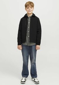 Svart jacka med ett blixtlåsfickor över en rutig skjorta, blå jeans och svart-vita sneakers, med en modern passform och rena linjer.