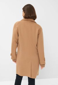 Manteau en mélange de laine marron avec un col cranté, des manches longues et des accents de boutons, présentant une coupe droite et une longueur mi-cuisse.