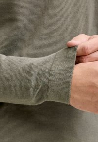 Tissu vert olive à manches longues présentant un tricot côtelé texturé. Le poignet est légèrement replié, révélant un matériau doux et lisse en dessous.