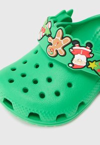 Tamanco verde com pendentes festivos de Natal, incluindo um homem de pão de gengibre, o Pai Natal, folhas de azevinho e uma estrela na tira.