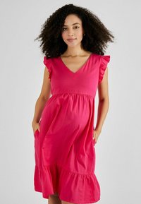 Rochie din bumbac roz, cu decolteu în V, mâneci volan și tiv în straturi. Are buzunare pe laterale și un design lejer, fluid.