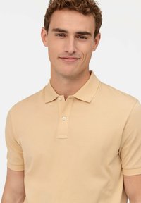 Beige Polohemd mit kurzen Ärmeln, einer knöpfbaren Blende und einem strukturierten Stoff. Einfaches Design, das sich gut für die Freizeit eignet.