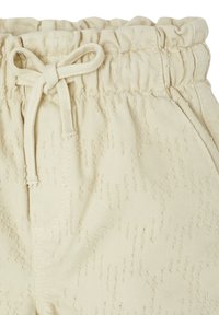 Cream-colored pants with a textured surface, featuring an elastic waistband and a drawstring closure. Two side pockets are visible.