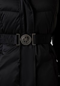 Fekete puffert G jacket textúrált övvel, kerek fém csattal. Az anyaga fényes és sima, az öv mentén ráncolt részletekkel.