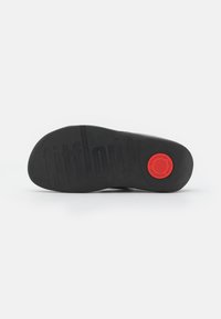 Black rubber sole with textured surface and "fitflop" logo. Features a prominent red circular accent and smooth edge.