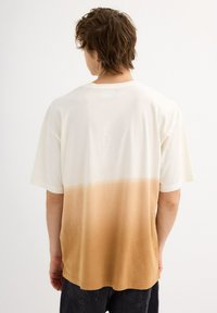 Camiseta de manga corta con un diseño en degradado, que va de crema a marrón claro, hecha de tela suave y con un corte holgado.
