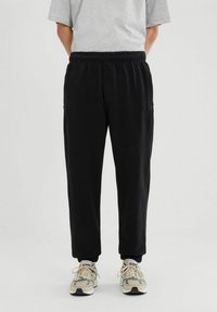 Czarne dresy z elastycznym pasem i mankietami na kostkach, z kieszeniami po bokach i miękką fakturą, w połączeniu z butami w neutralnych odcieniach.