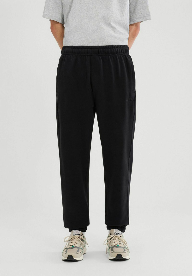 Czarne dresy z elastycznym pasem i mankietami na kostkach, z kieszeniami po bokach i miękką fakturą, w połączeniu z butami w neutralnych odcieniach.