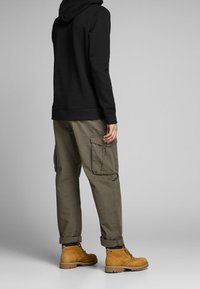 Schwarzes Kapuzensweatshirt, olivgrüne Cargo-Hosen mit seitlichen Taschen und beigefarbene Arbeitsschuhe mit Schnürsenkeln; lockere Passform und hochgekrempelte Hosenbeine.