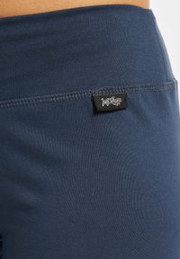 Marineren stretchlegging in navy blauw met een gladde textuur en een zichtbaar label met "Just Rhye." De stiksels langs de tailleband zijn netjes afgewerkt.