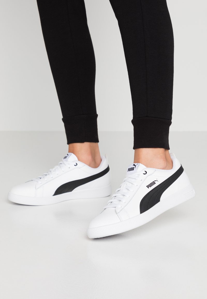 Weiße Sneakers mit schwarzem Akzentstreifen, glattem Synthetik-Obermaterial, runder Zehenpartie, Schnürdesign und strukturiertem Gummisohle. Puma-Logo an der Seite.