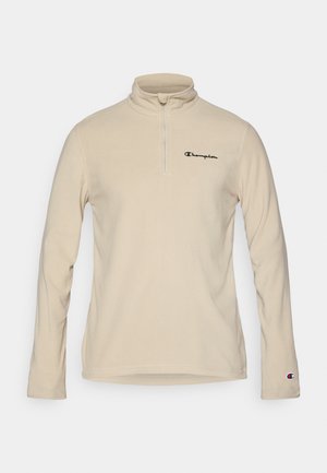 Pulover din fleece bej cu guler înalt, închidere cu jumătate de fermoar și logo-ul negru "Champion" pe piept. Mânecile lungi au un accent cu logo pe mansetă.