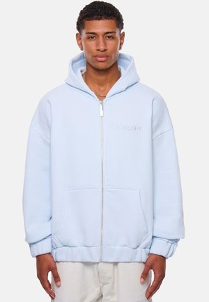 Light blue zip-up hoodie made from soft fabric, featuring a large hood, ribbed cuffs, kangaroo pockets, and embroidered logo on the chest.
