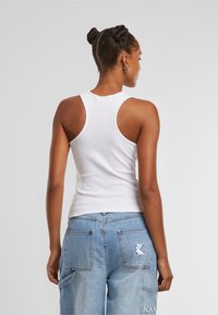 Débardeur blanc à côtes avec un dos nageur, associé à un jean cargo bleu clair avec deux poches arrière et un détail de logo.