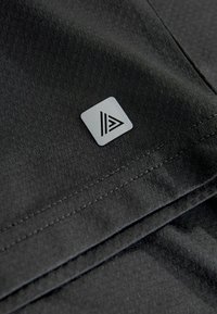 Schwarzer Stoff mit glatter Textur, versehen mit einem kleinen, quadratischen grauen Etikett, das in der unteren Ecke mit einem dreieckigen Design geprägt ist.