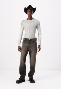 Grå ribbet langermet skjorte paret med løse, mørkegrå jeans og svarte kraftige støvler. Modellen har på seg en svart cowboyhatt.