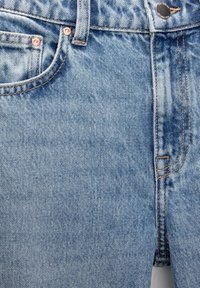 Jean en denim bleu clair avec une texture délavée, doté de rivets et de coutures couleur cuivre, une poche avant, et un design classique.