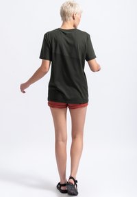 Olijfgroen t-shirt met korte mouwen en ronde hals, gemaakt van zachte stof. De achterkant heeft een subtiele logodetail en is gecombineerd met rode shorts.