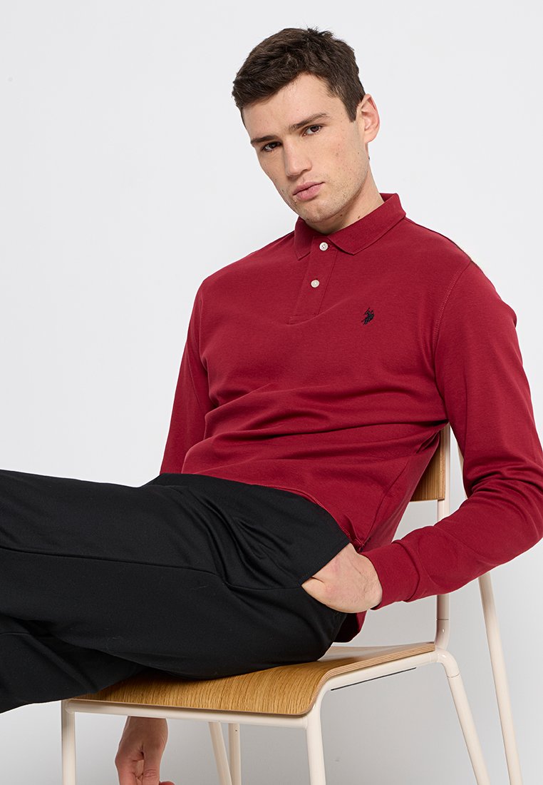 Polo à manches longues bordeaux avec une patte de boutonnage à trois boutons et un petit logo brodé sur la poitrine, associé à un pantalon noir ajusté.