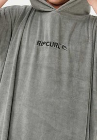Szary, kapturowy poncho wykonane z miękkiego, teksturowanego materiału. Charakteryzuje się wyraźnym czarnym logo "RIPCURL" z przodu, które identyfikuje markę.