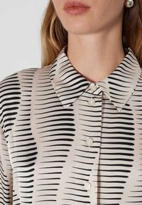 Blouse featuring a light beige fabric with black horizontal stripes, a pointed collar, and classic button details.