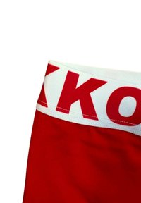 Röda idrottsshorts med ett vitt elastiskt midjeband som har röda "K"-bokstäver. Tyget verkar slätt med en lätt glans.