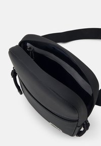 Black crossbody bag made from textured material, featuring a zip closure and single shoulder strap; interior is lined with solid fabric.
