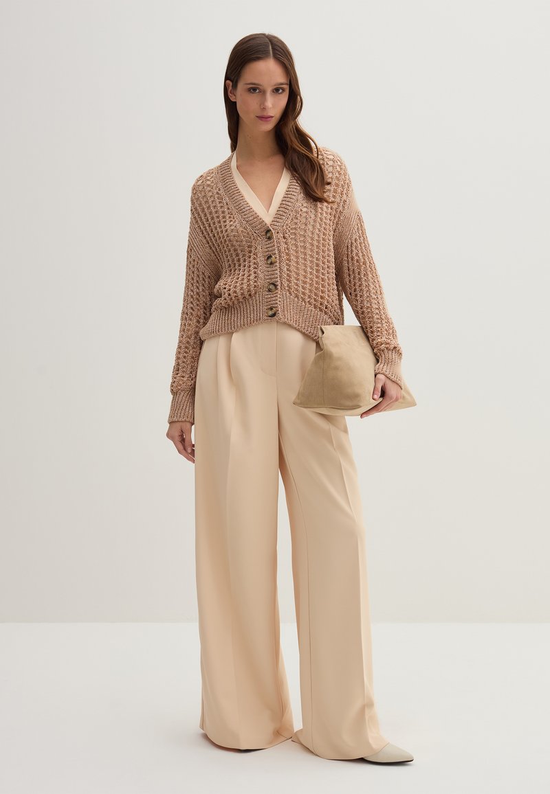 Beżowy sweter dziany z guzikami, zestawiony z luźnymi, jasnobeżowymi spodniami oraz miękką, taupe torebką kopertową. Neutralne kolory i fakturowany materiał.