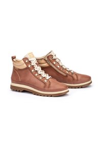 Botas de tobillo de cuero marrón con un acabado texturizado, cordones crema, cremallera lateral y una suela de goma marrón con un patrón de tracción robusto.