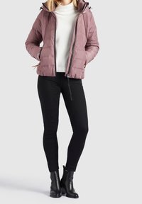 Vadderad, lätt rosa jacka med huva, framdragkedja och elastiska ärmslut. Kombinerad med svarta åtsittande byxor och svarta hälsodelar.