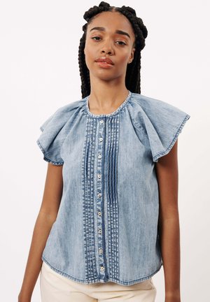 Blouse en denim bleu clair avec des manches courtes à volants, fermeture à boutons à l'avant, et plis verticaux, présentant un col rond et une coupe décontractée.