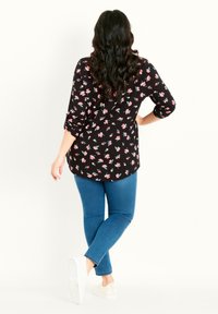 Blusa nera a fiori con disegni rosa e blu, maniche lunghe risvoltate, orlo arrotondato, abbinata a jeans blu e sneakers chiare.