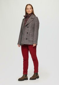 Grau doppelt geknöpfter Fischgrätenmantel, getragen über einer burgunderfarbigen Daunenjacke. Kombiniert mit roten Cordhosen und braunen Stiefeletten.