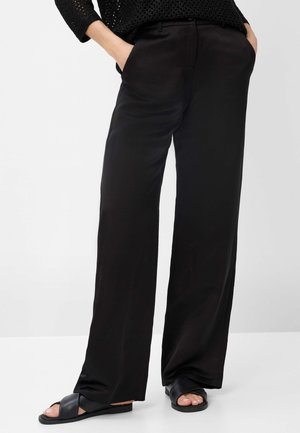 Pantaloni neri a gamba larga in materiale liscia con tasche laterali. Abbinati a sandali neri a pianta piatta con fascette incrociate. Design semplice e minimalista.
