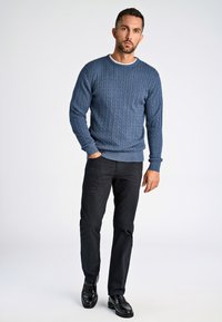 Blauer Kabelstrickpullover mit Rundhalsausschnitt, kombiniert mit schwarzen Hosen und glänzenden schwarzen Schuhen. Der Pullover weist ein strukturiertes, geripptes Design auf.