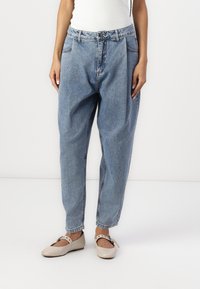 Blå denim jeans med en løs pasform, høj talje og sidelommer. Båret med beige flade sko med rem og dekorativ spænde.