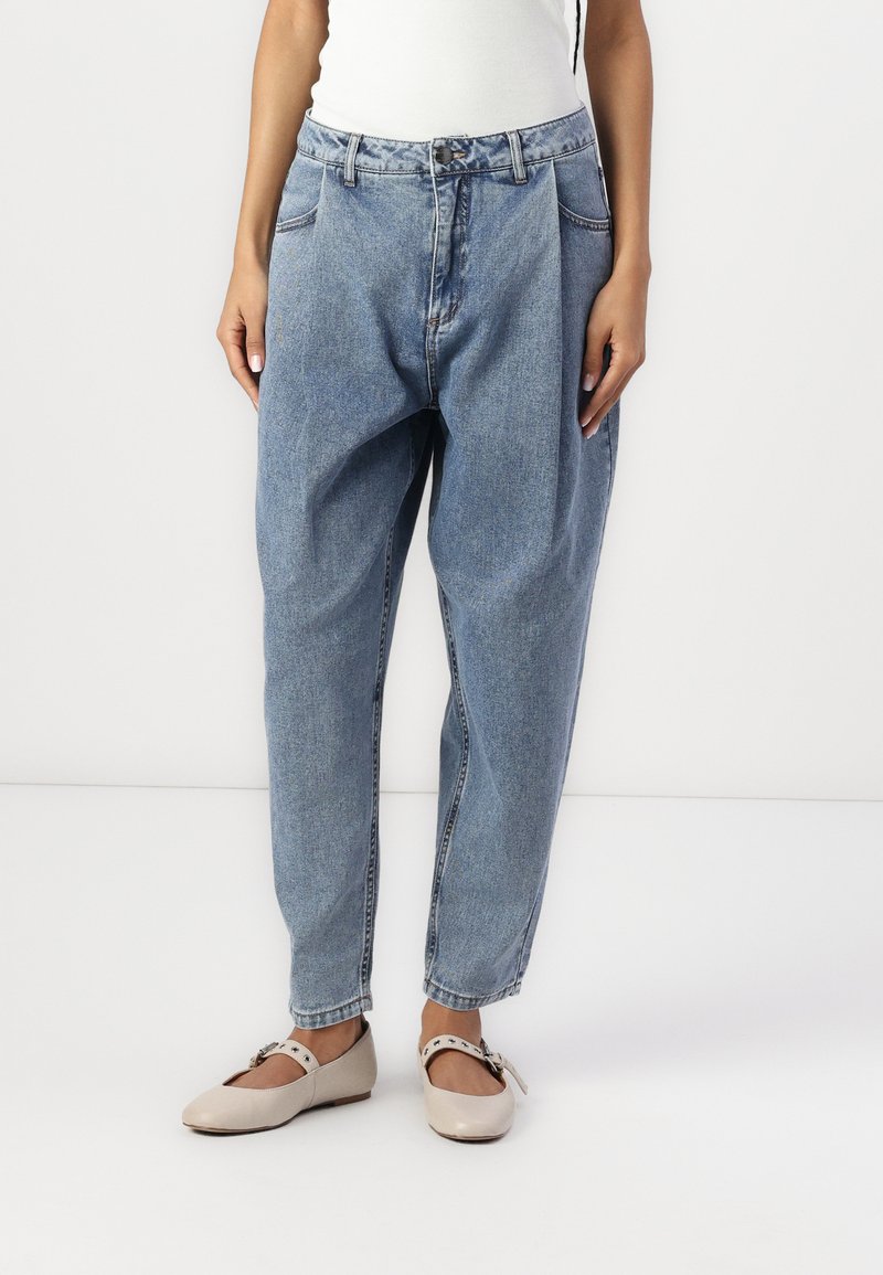 Blå denim jeans med en løs pasform, høj talje og sidelommer. Båret med beige flade sko med rem og dekorativ spænde.