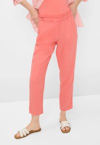 Koraal kleurige linnen broek met een gerimpelde elastische tailleband, taps toelopende benen en opgerolde manchetten, gecombineerd met beige platte sandalen.