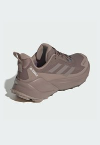Trailrunningschuh in Taupe, mit einer strukturierten Oberseite, einem Schnürsystem und einer dicken Gummisohle mit tiefen Profilierungen für besseren Halt.