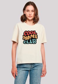Cream-colored cotton t-shirt featuring a bold, multi-colored graphic print stating "COOL MOMS CLUB" in playful, varying fonts.