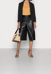 Czarne kuloty z sztucznej skóry w połączeniu z musztardową bluzką, czarnym żakietem, brązowymi sandałami na słupku i plecioną torebką.