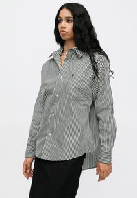 Schwarz-weiße gestreifte Langarmbluse mit Kragen, Knopfverschluss vorne und einer Brusttasche. Sie hat einen abgerundeten Saum und kontrastierende Manschetten.