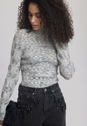Grijze geblokte longsleeve top met een hoge hals, gecombineerd met een hoge taille zwarte jeans met gekleurde franjes.