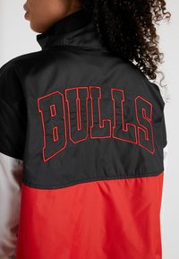 Svart och röd vindjacka med "BULLS" broderat i fet stil på baksidan, med en slät textur och kontrasterande blockdesign.