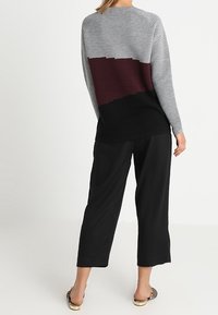 Pull côtelé léger avec un haut gris, un milieu rouge vin et un bas noir. Associé à un pantalon noir ample et des chaussures à motifs.
